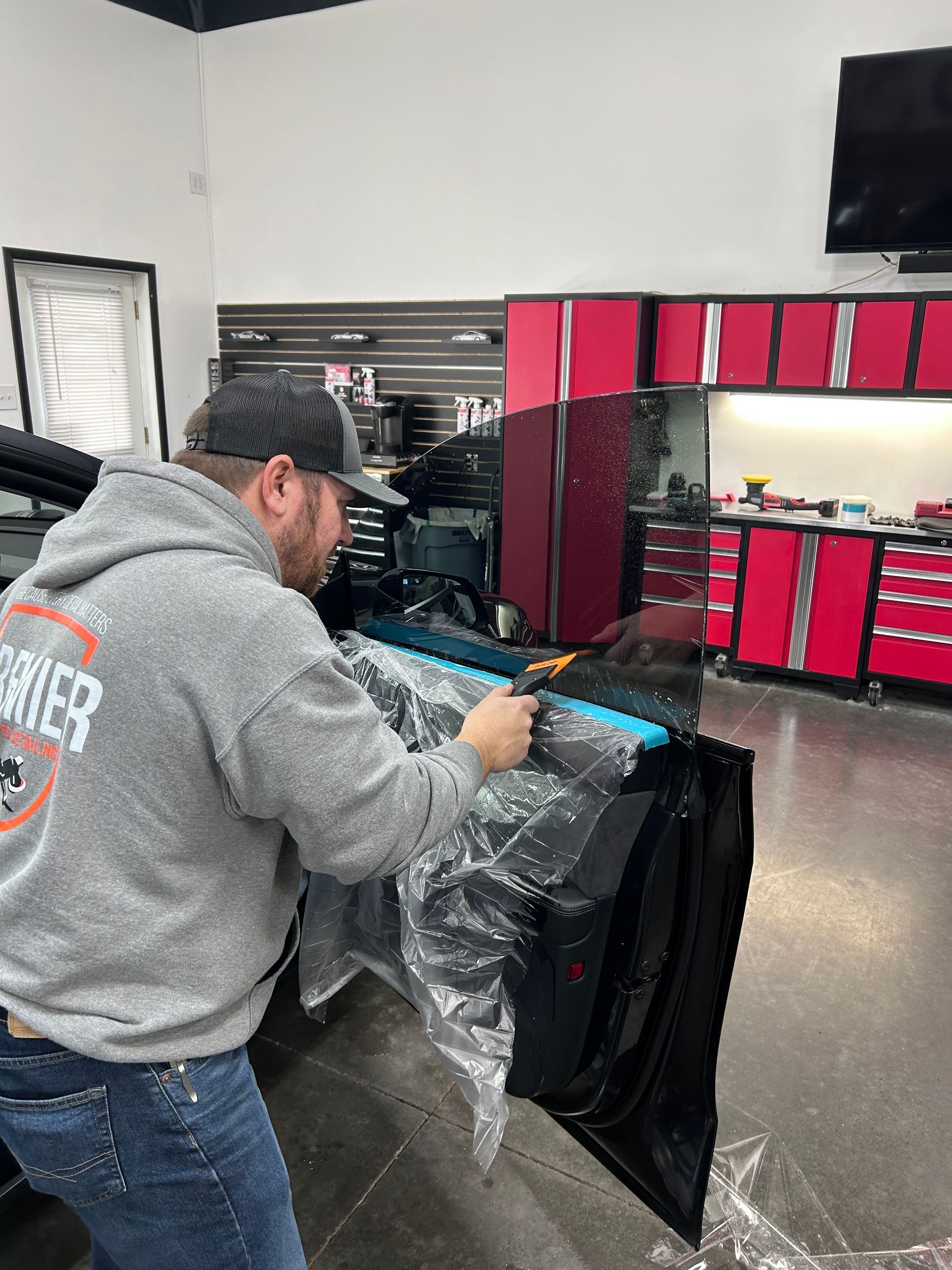 Man applying tint to a car window inside a shop, using a squeegee.