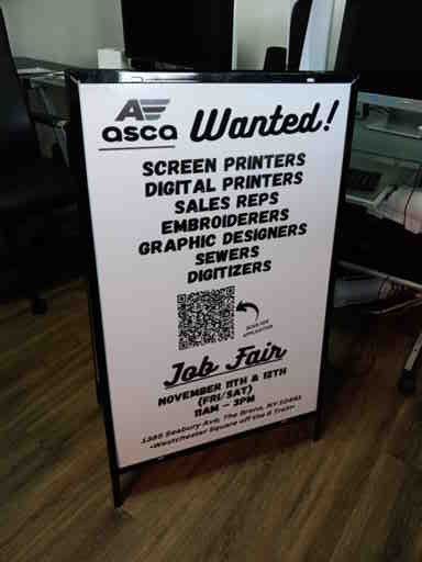 A sign that says `` screen printers wanted '' is sitting on a wooden floor.
