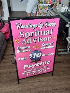 A pink sign for readings by bubbly spiritual advisor is sitting on a wooden floor.