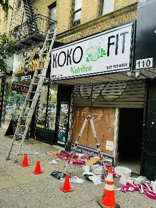A ladder is sitting on the sidewalk in front of a store that is being remodeled.