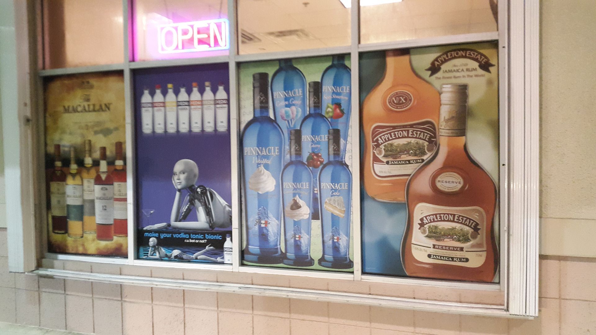 A window with bottles of alcohol on it and a sign that says open