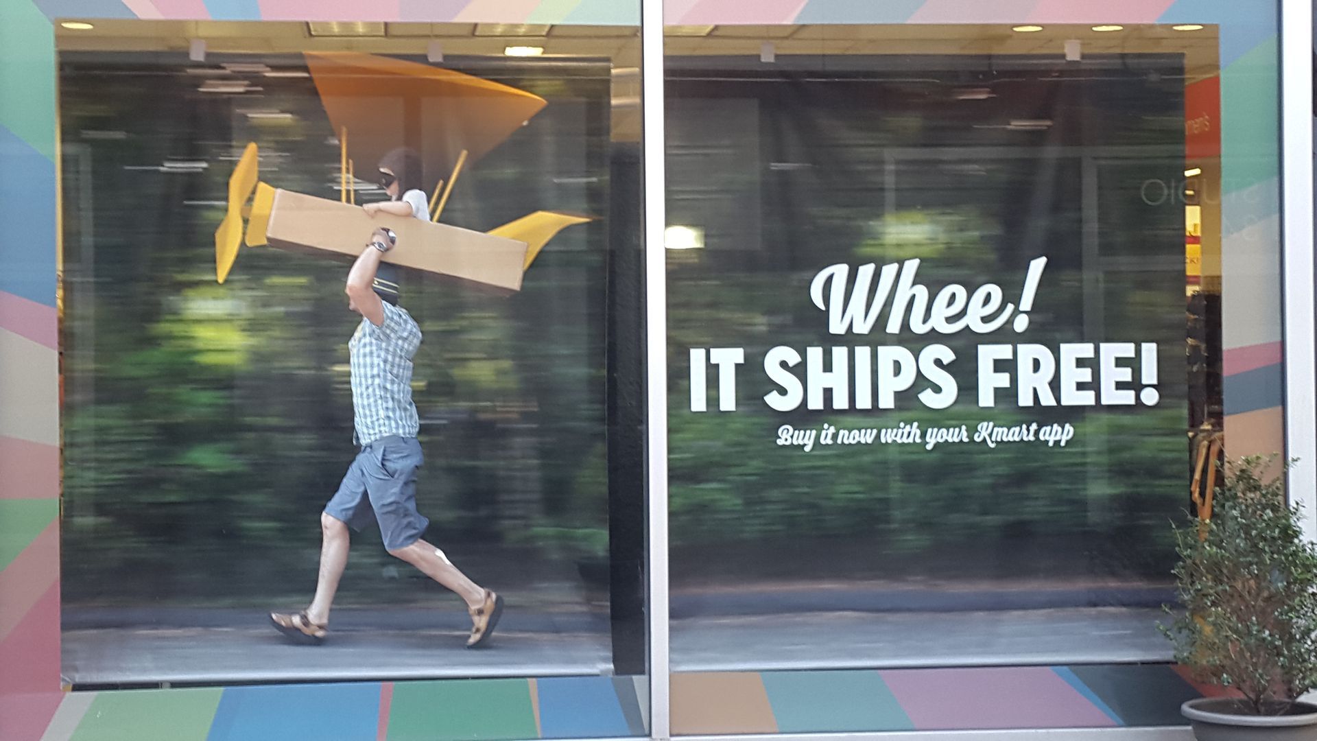 A man is carrying a model airplane in front of a sign that says whee it ships free
