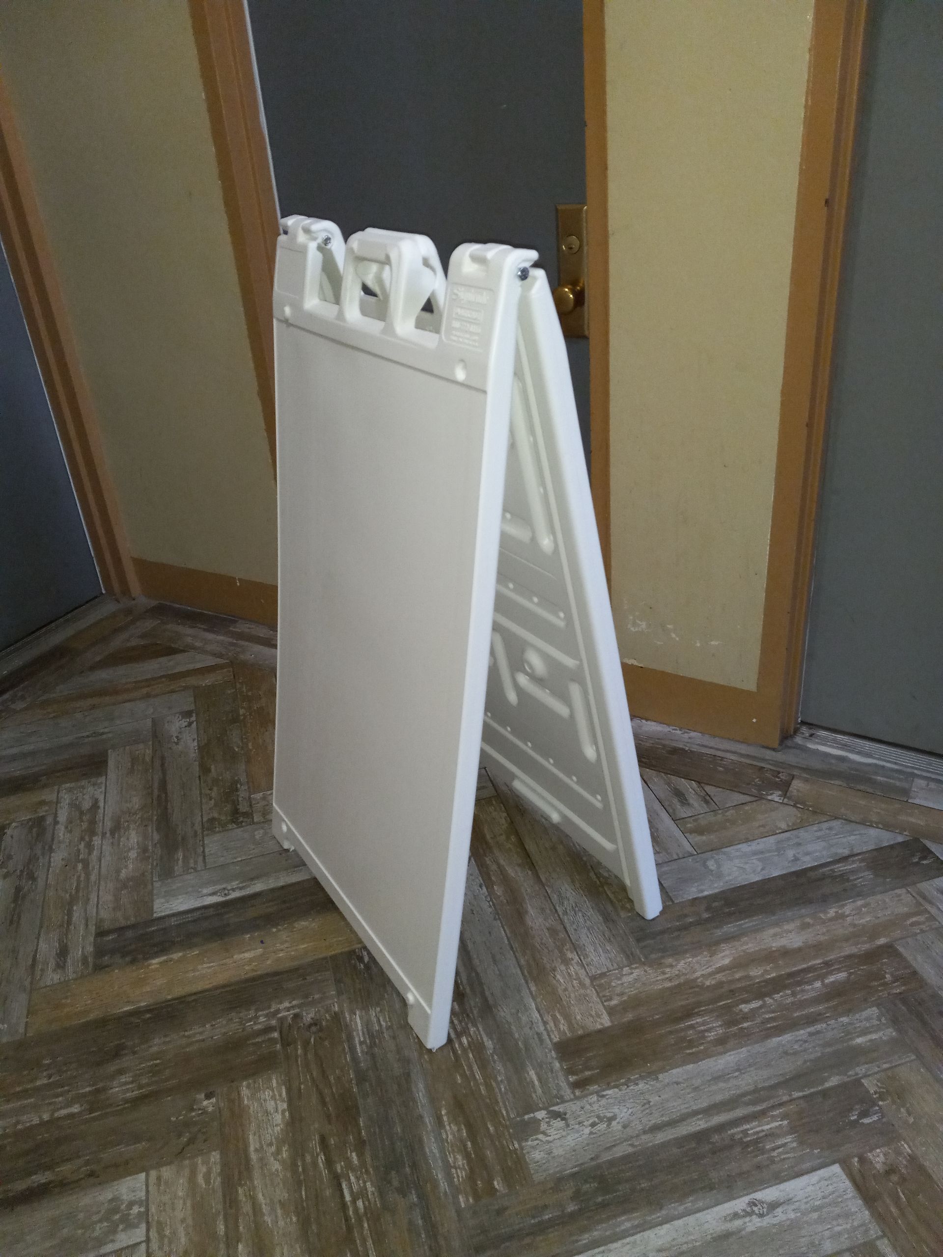 A white sign is sitting on a wooden floor.