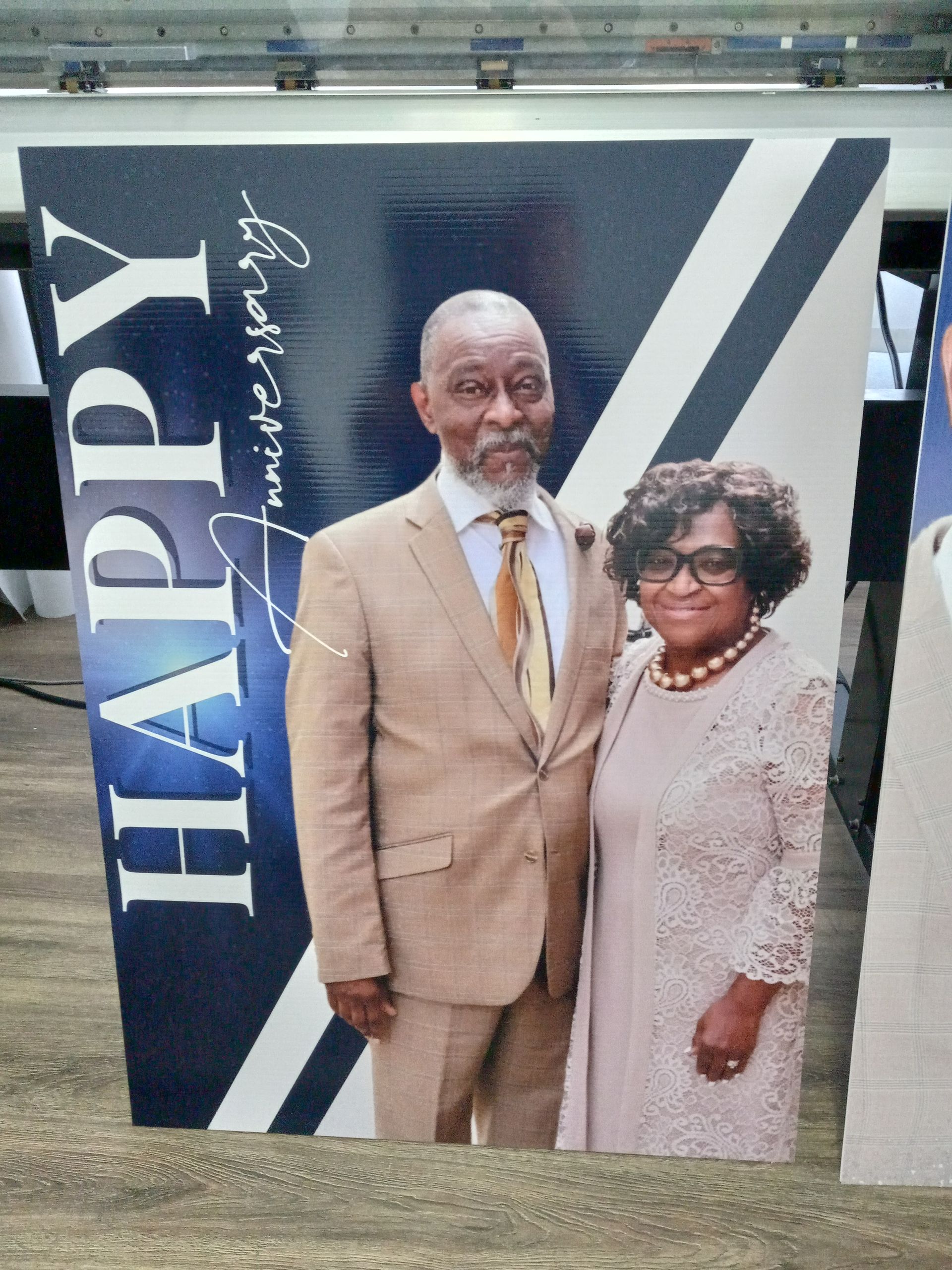 A man and woman are standing next to each other in front of a sign that says happy anniversary