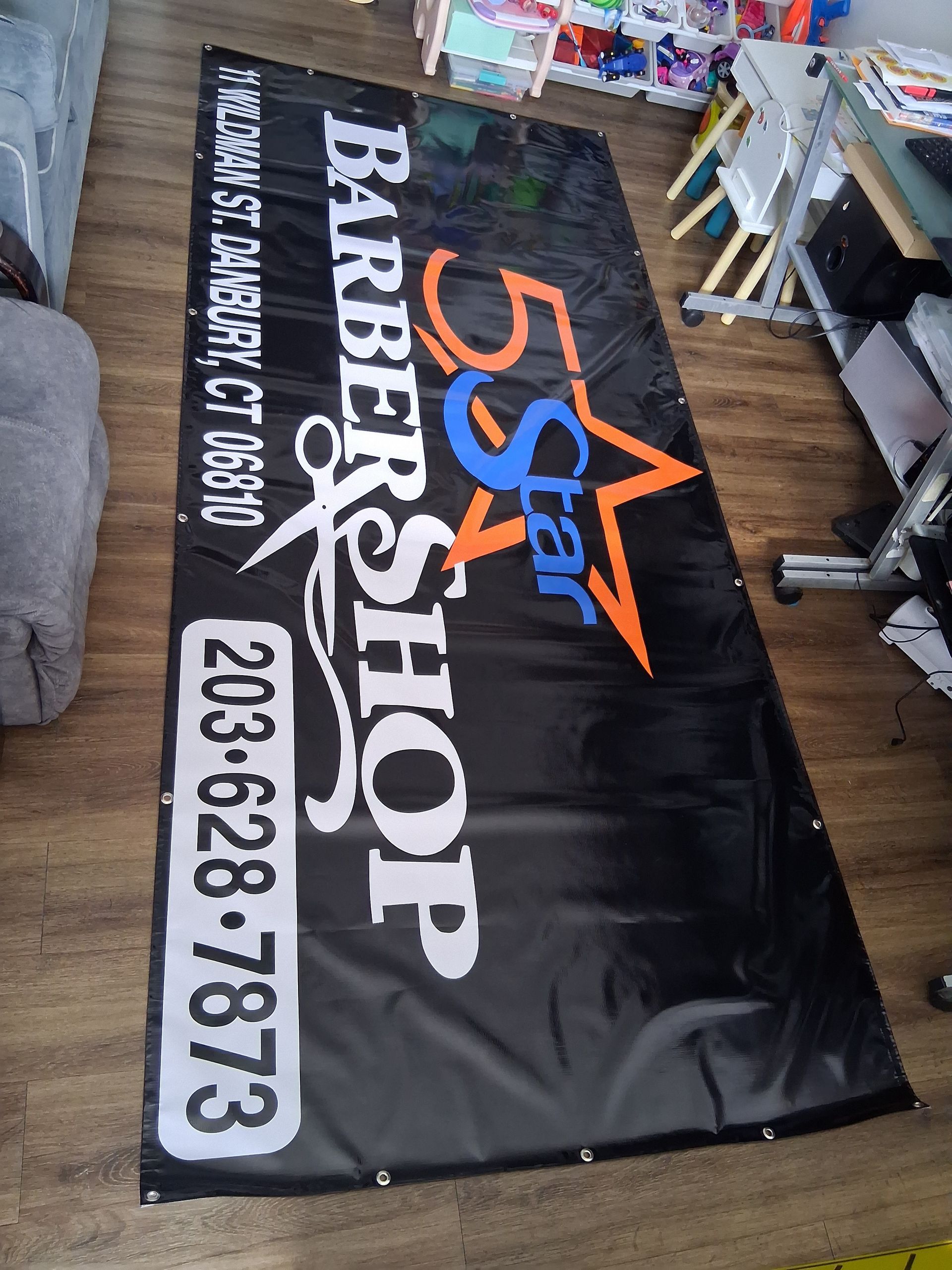 A banner for a barber shop is sitting on a wooden floor