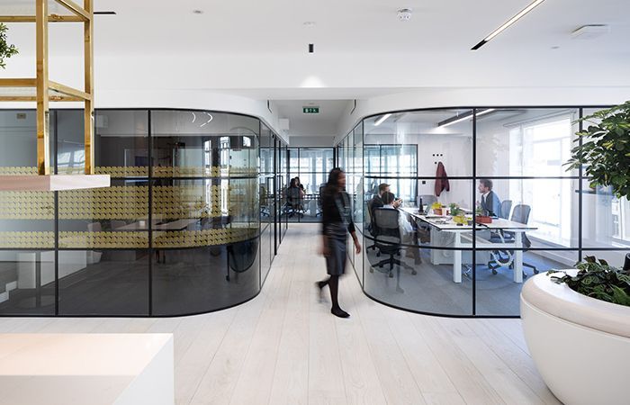 A woman is walking through an office with a lot of glass walls.