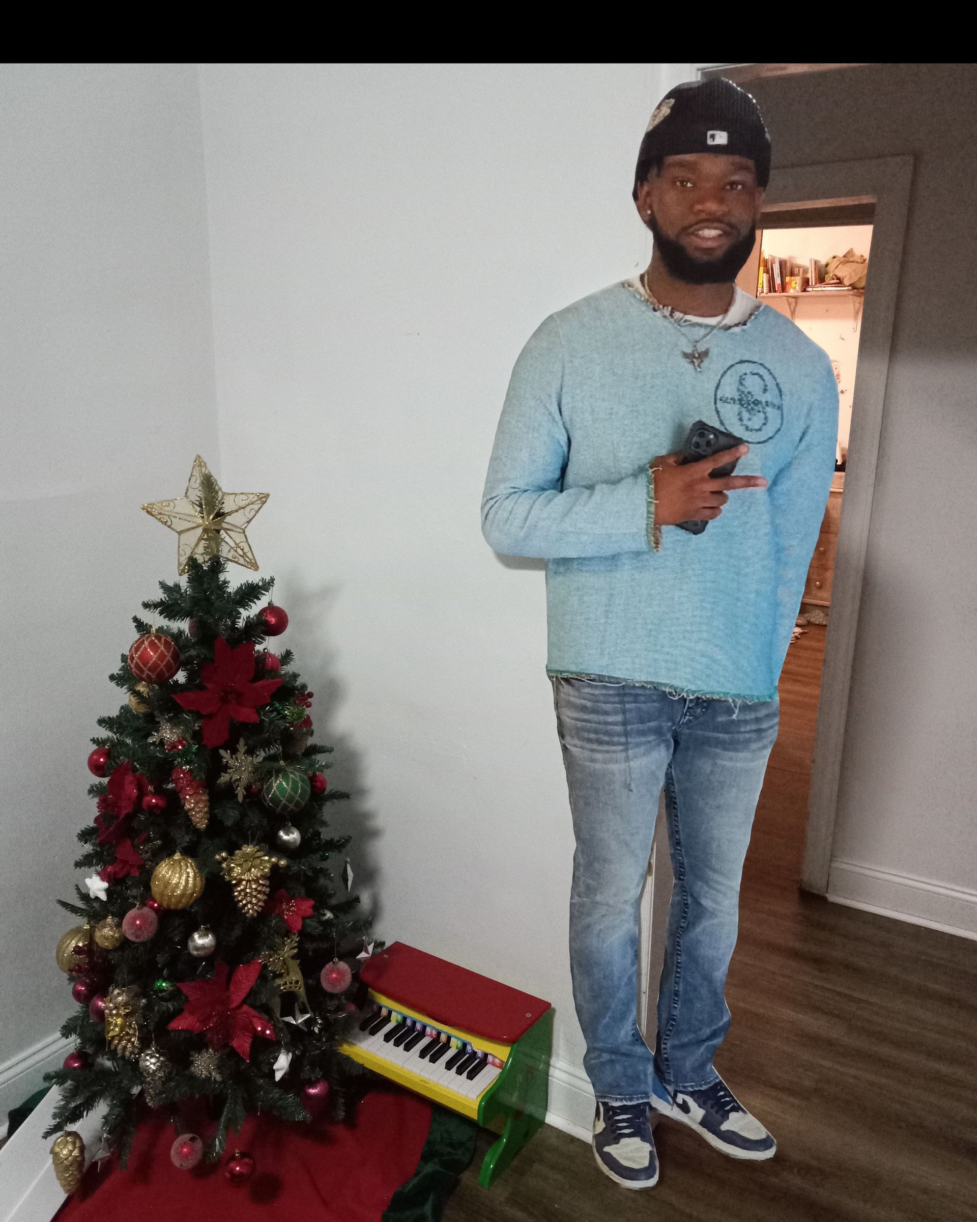 A man in a blue sweater is standing in front of a christmas tree