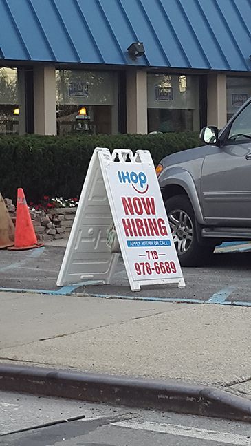A car is parked in front of a sign that says now hiring