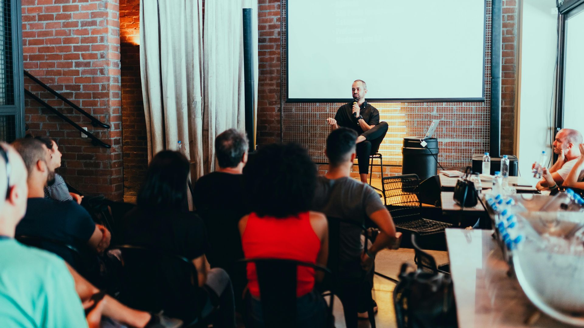 A group of people are sitting in front of a projector screen in a room.