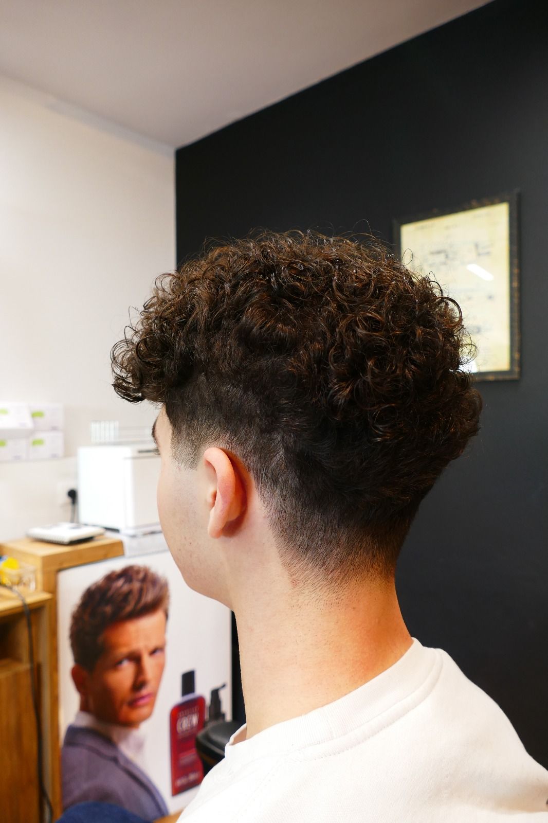 Uomo con capelli ricci e un taglio di capelli sbiadito, visto di spalle, in un salone di bellezza.