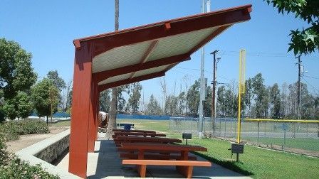 A row of wooden picnic tables under a canopy in a park