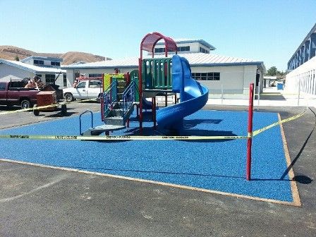 A playground with a blue slide and stairs in a parking lot