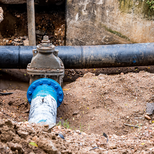 A blue and white pipe is sitting in the dirt next to a black pipe.