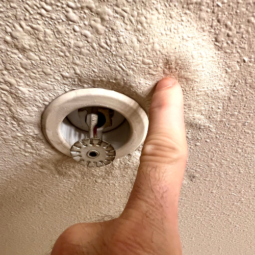 A person is pointing at a fire sprinkler on the ceiling.