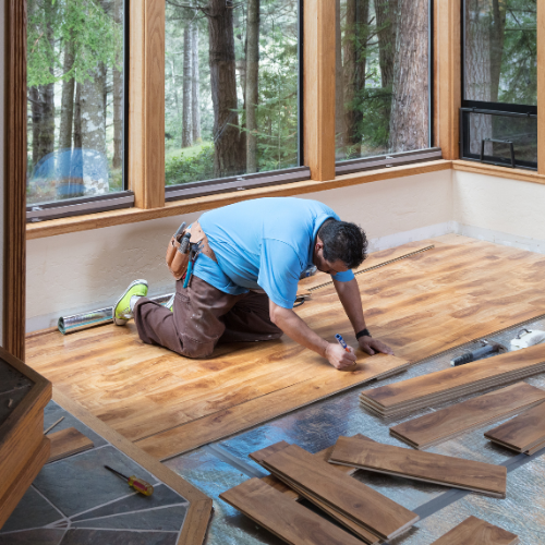 A man is kneeling on the floor while installing a wooden floor