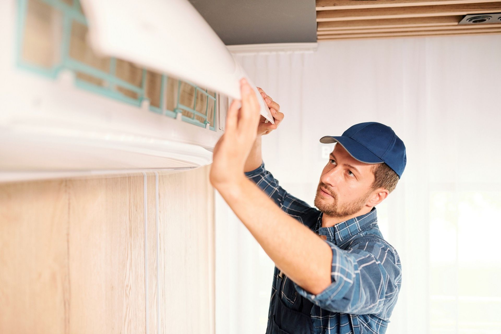 Technician installing a wall-mounted air conditioner indoors, reaching up with tools.