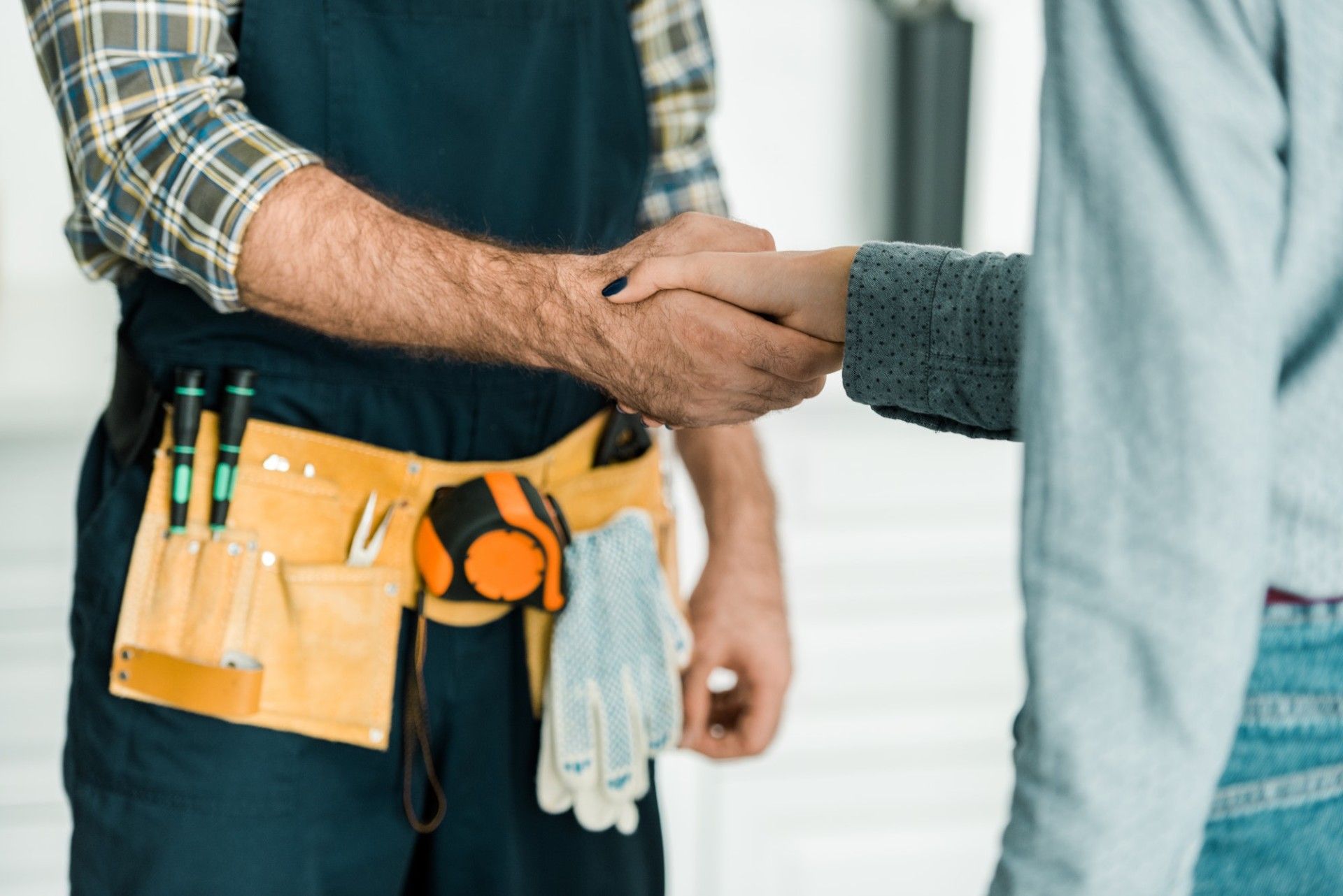 A worker in a tool belt shaking hands with a person indoors