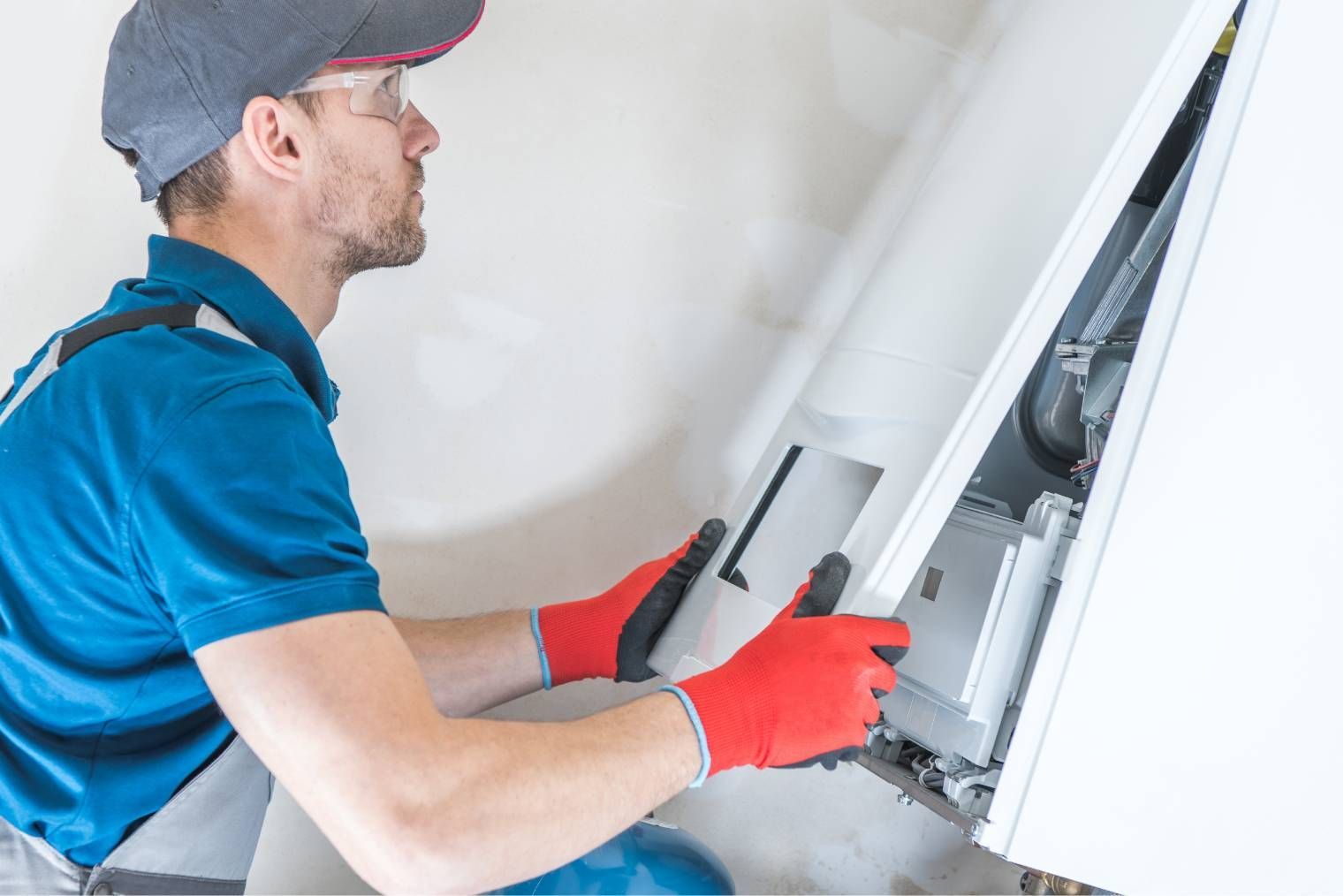 Technician in blue shirt and red gloves inspecting an open wall-mounted unit with a screwdriver