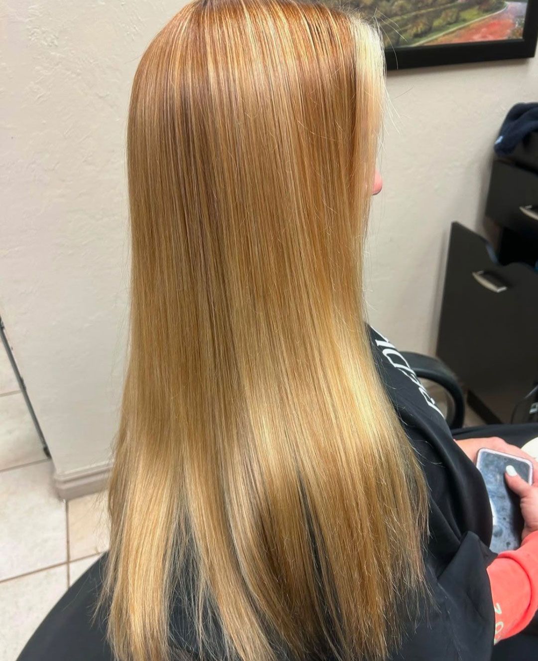 Woman with long, straight, light-brown hair, possibly styled. Seated in a salon chair.