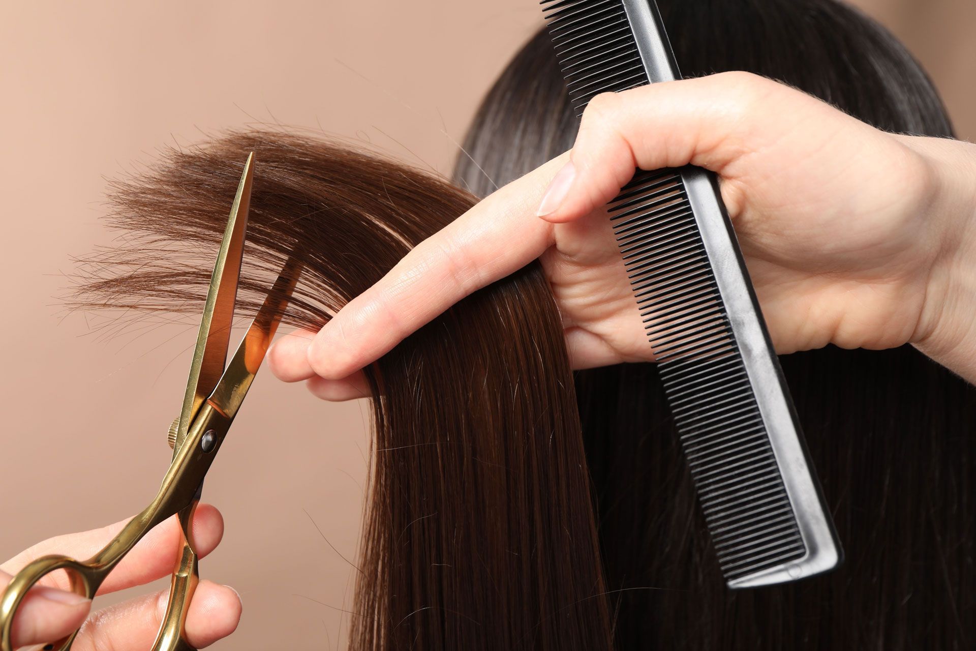 Hair stylist cutting dark hair with gold scissors and a comb.