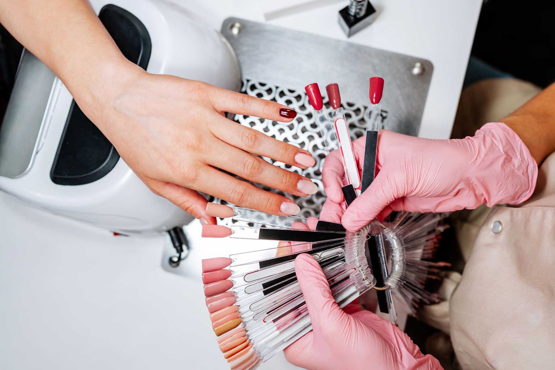 Person selecting a nail polish color from a sample fan during a manicure.