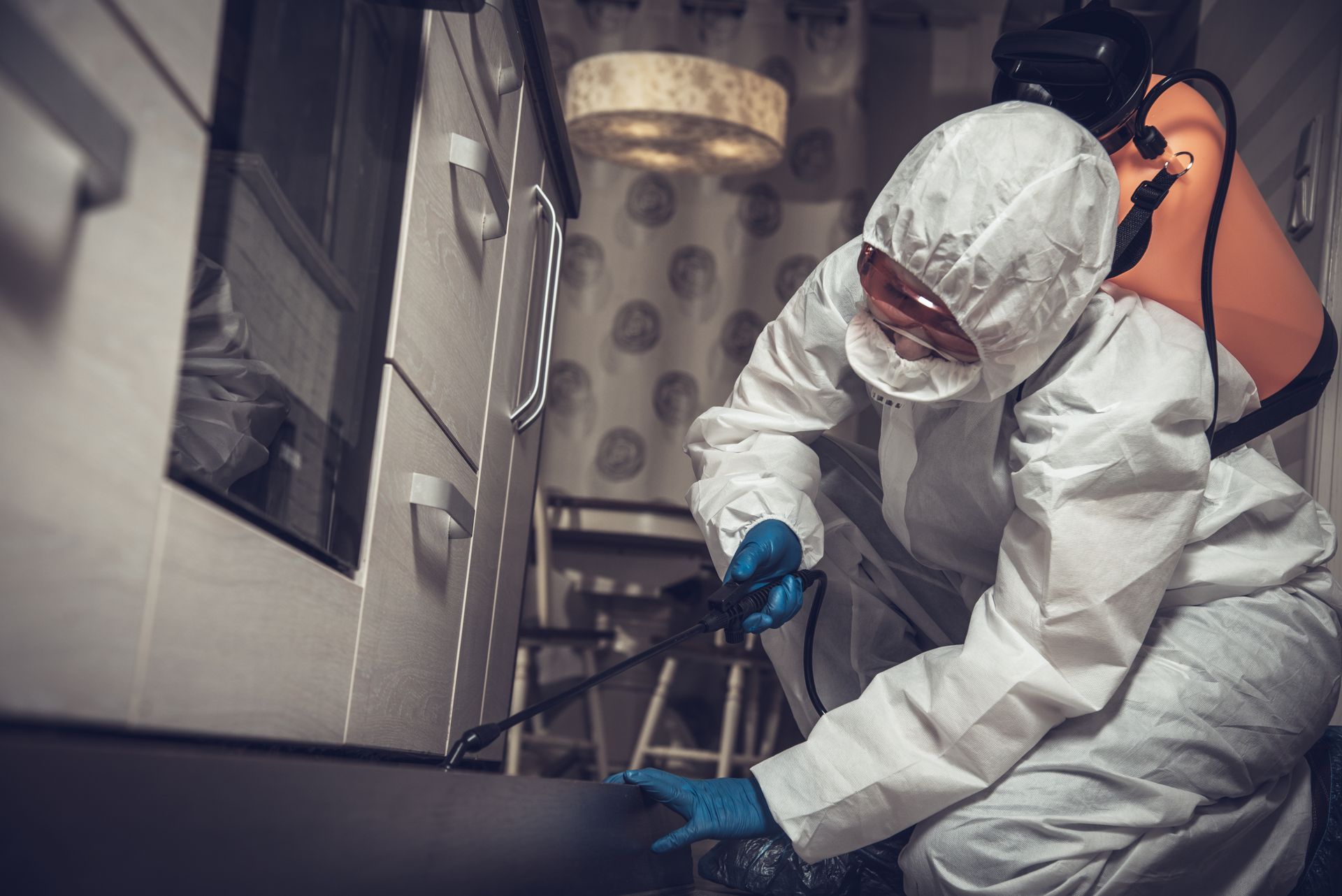 Person in protective suit spraying insecticide in a kitchen.