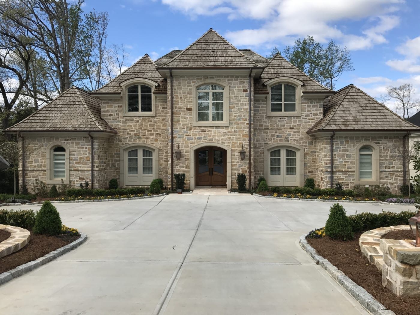A large stone house with a concrete driveway in front of it
