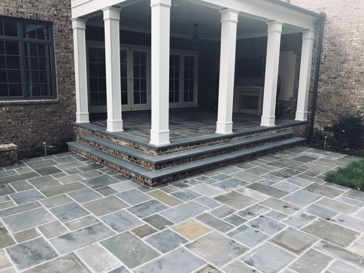 A stone patio with steps and a porch in front of a brick house