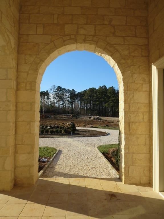A stone archway leading to a driveway with trees in the background