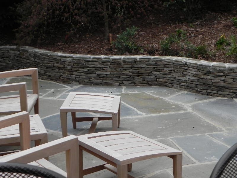 A patio with chairs and ottomans and a stone wall