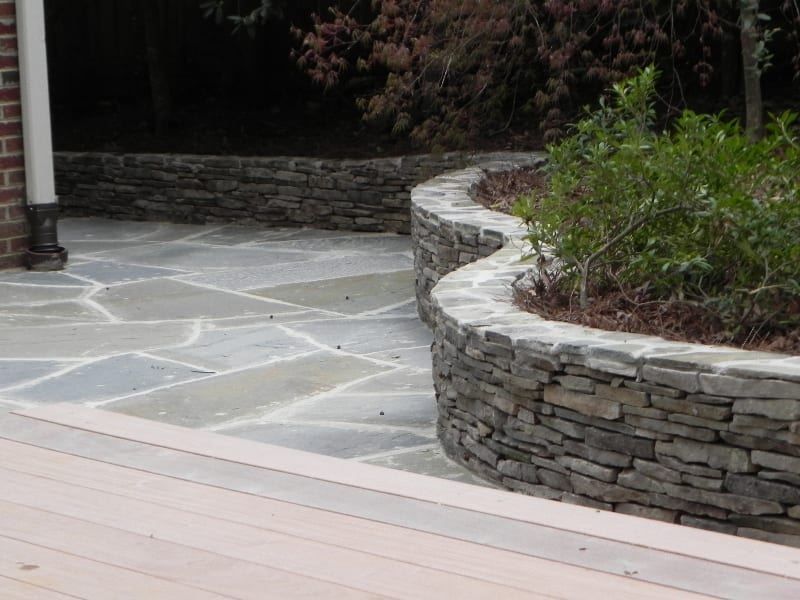 A stone wall surrounds a patio with a brick building in the background