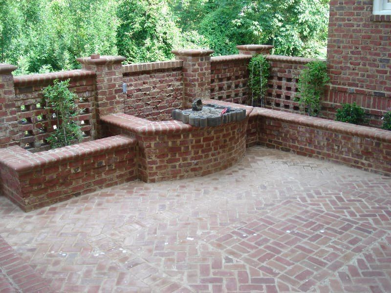 A brick patio with a bench and a fountain in the middle