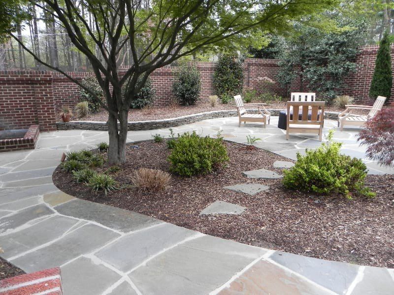 A stone patio with chairs and a tree in the middle