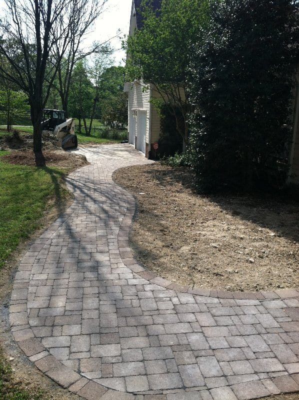 A brick walkway leading to a house with a bulldozer in the background.