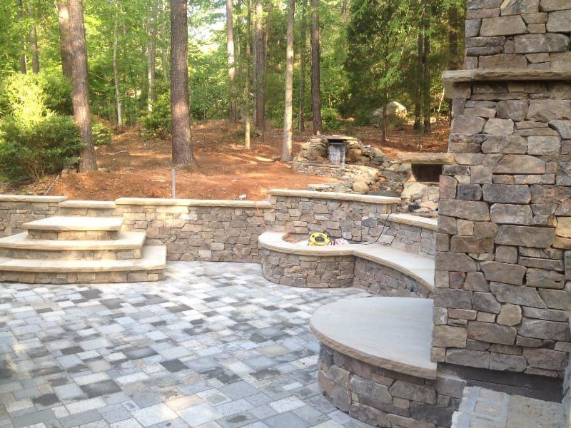 A stone patio with a fireplace and steps in the woods