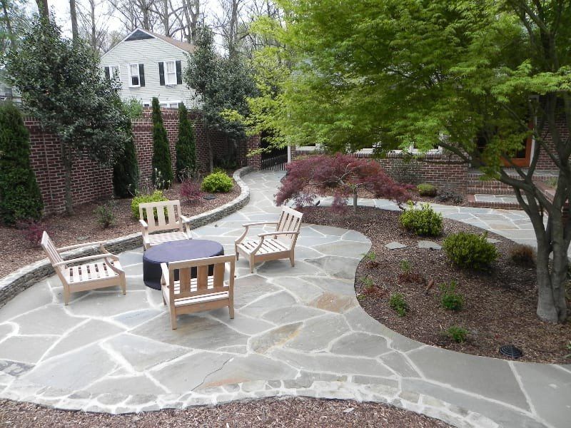 A stone patio with chairs and a table in a garden
