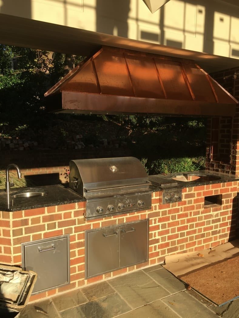 A brick outdoor kitchen with a copper hood and a grill