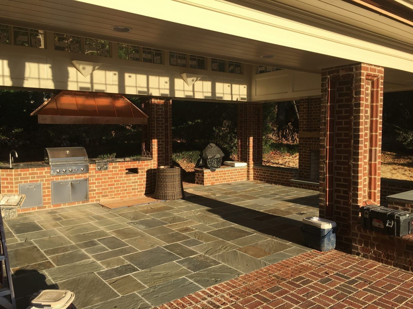 A brick patio with a grill and a cooler underneath it
