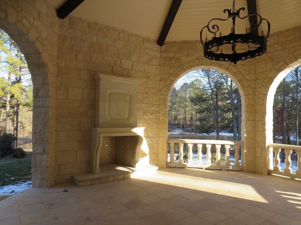 An empty porch with a fireplace and a chandelier hanging from the ceiling