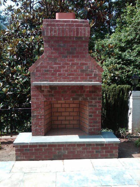 A brick fireplace is sitting on a patio with trees in the background