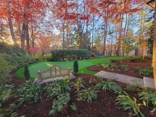 A putting green in the middle of a forest with a bench in the foreground