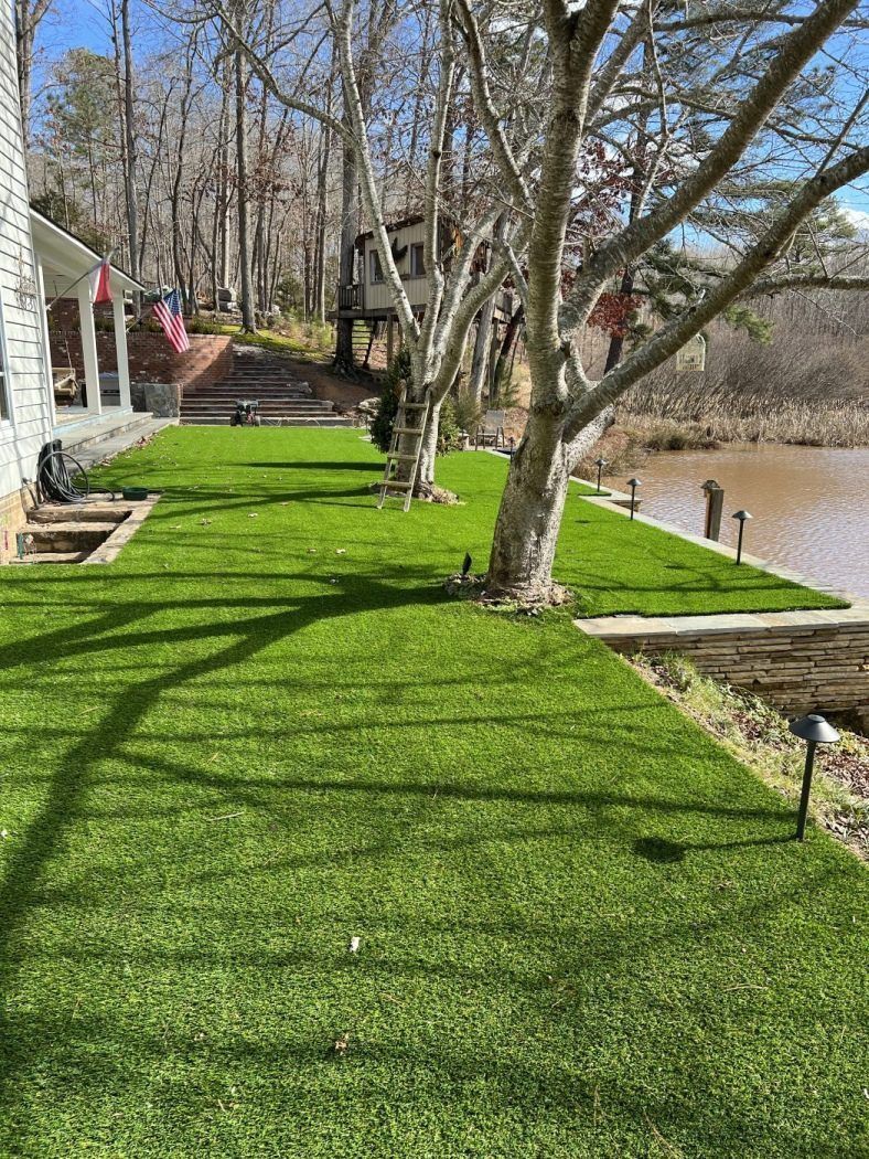 A lush green lawn in front of a house next to a lake