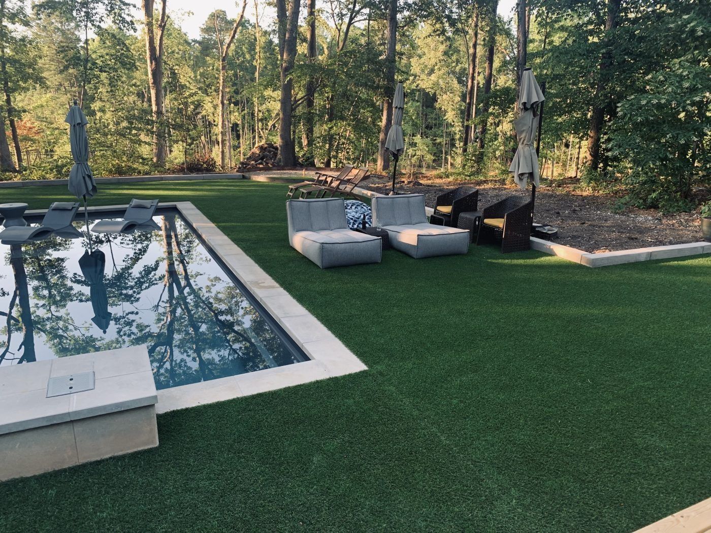 A swimming pool surrounded by a lush green lawn with chairs and umbrellas