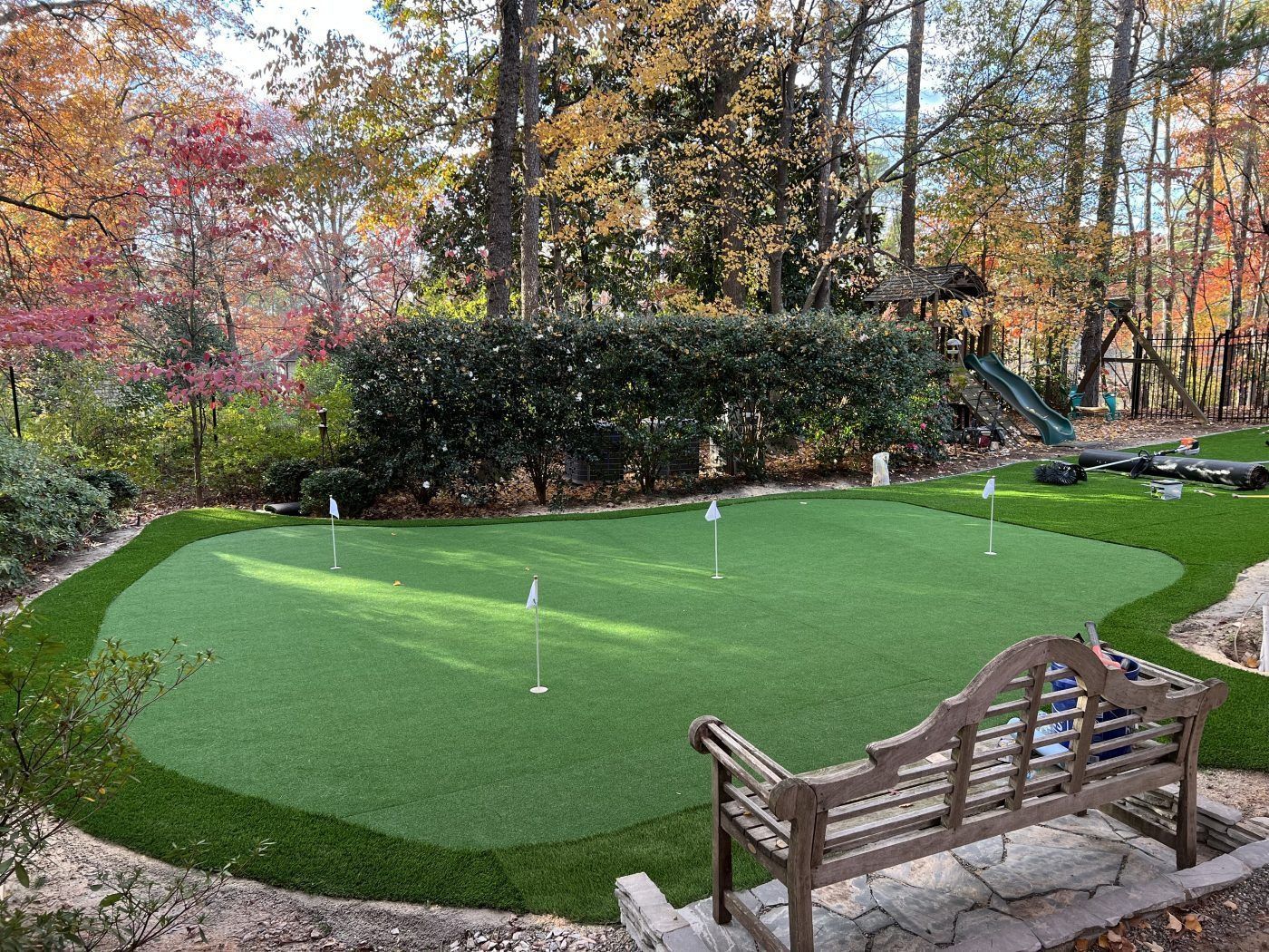 A putting green in a backyard with a bench in the middle of it