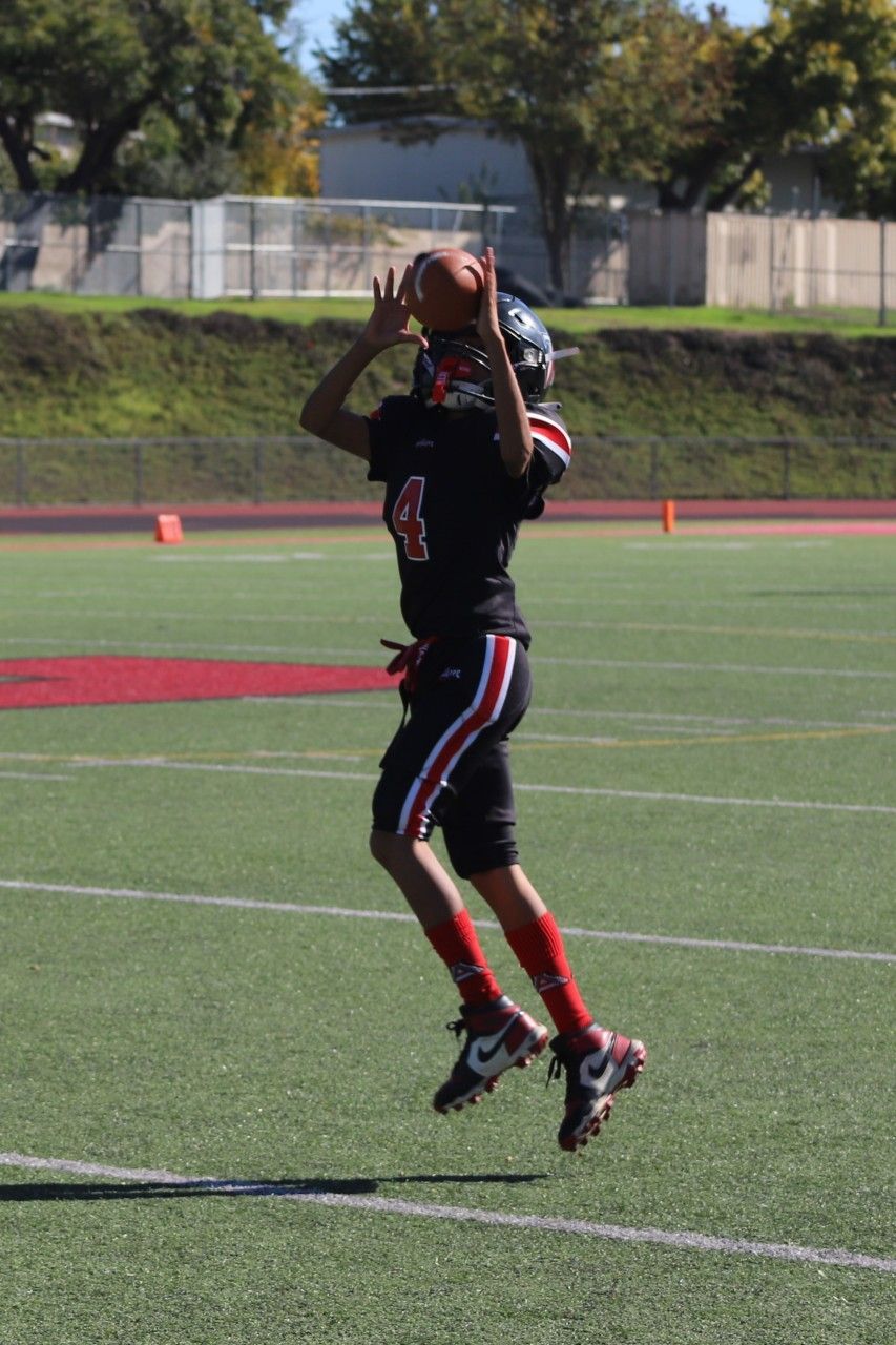 Football player in maroon jersey holding ball, smiling, surrounded by teammates on a field.