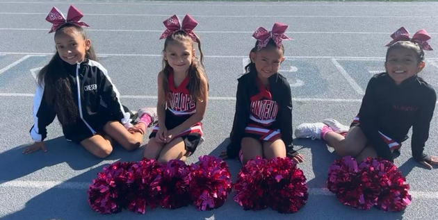 Cheerleader in red uniform performs a backbend on a green and red football field.