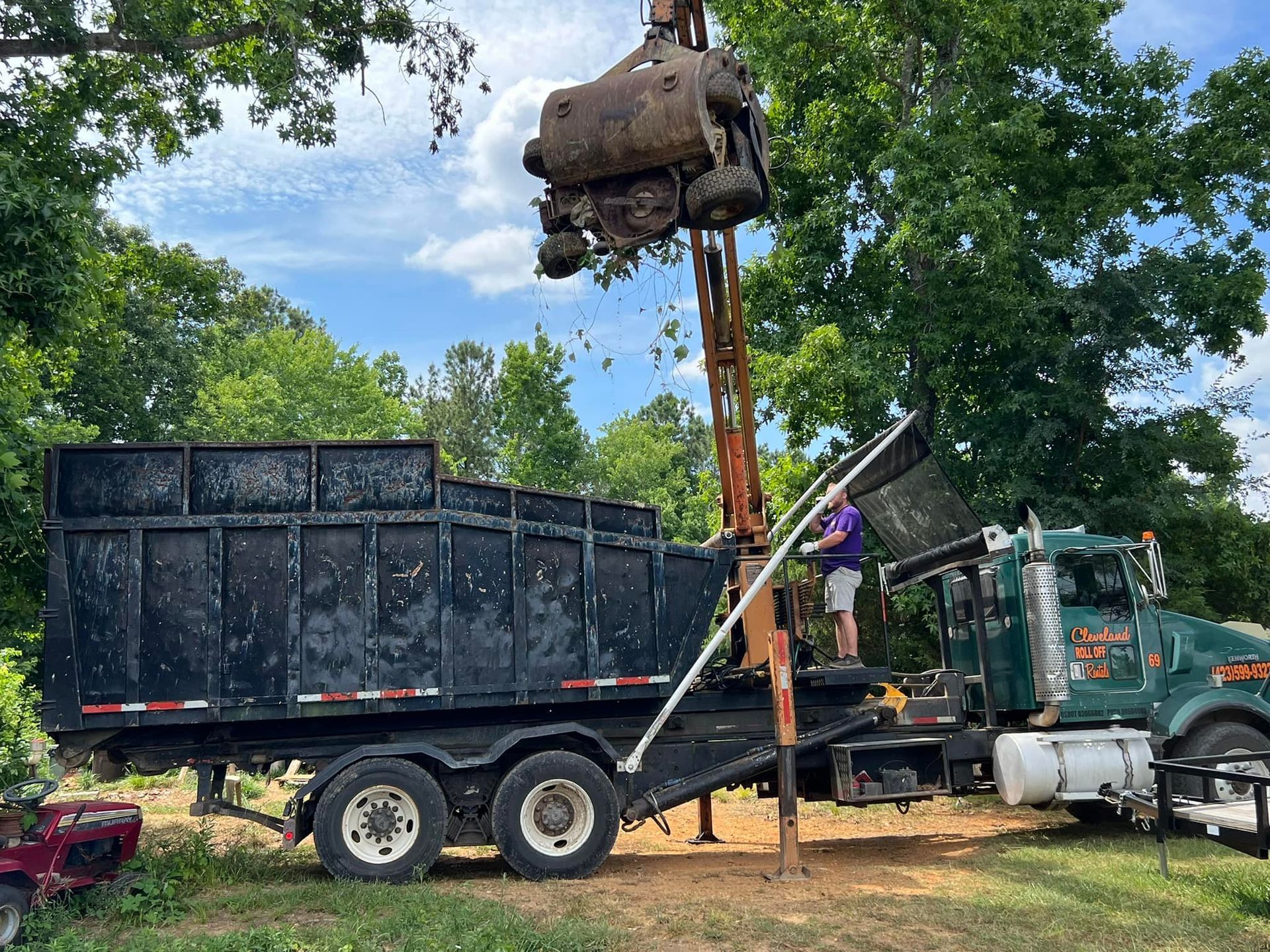 A truck loading debris into a large black container with a mechanical arm on a sunny day.