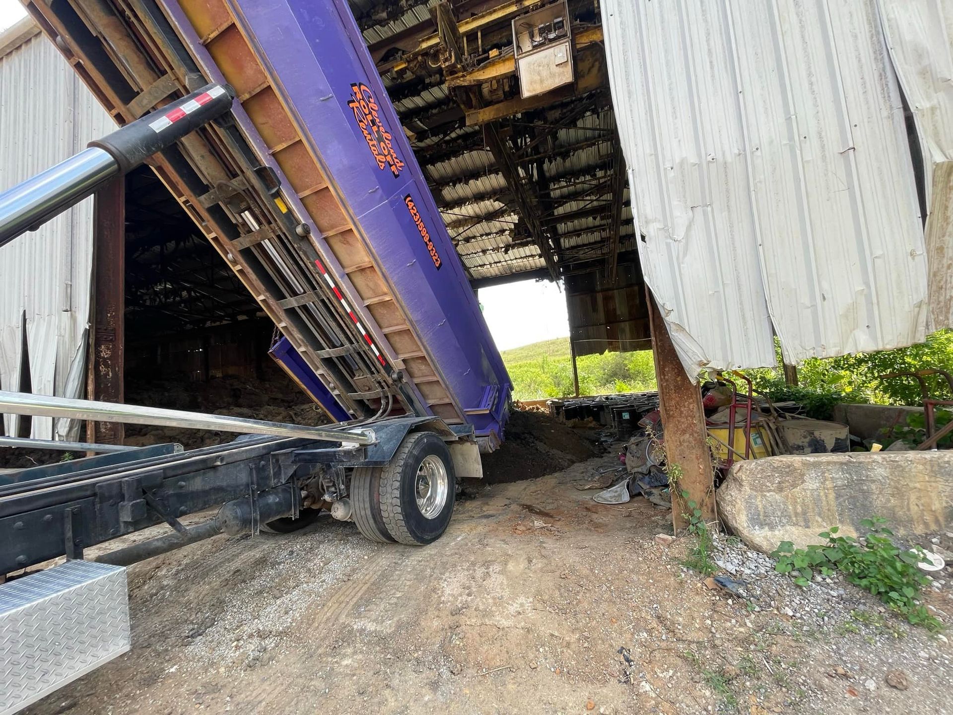 A purple dump truck inside a damaged white building, unloading gravel.