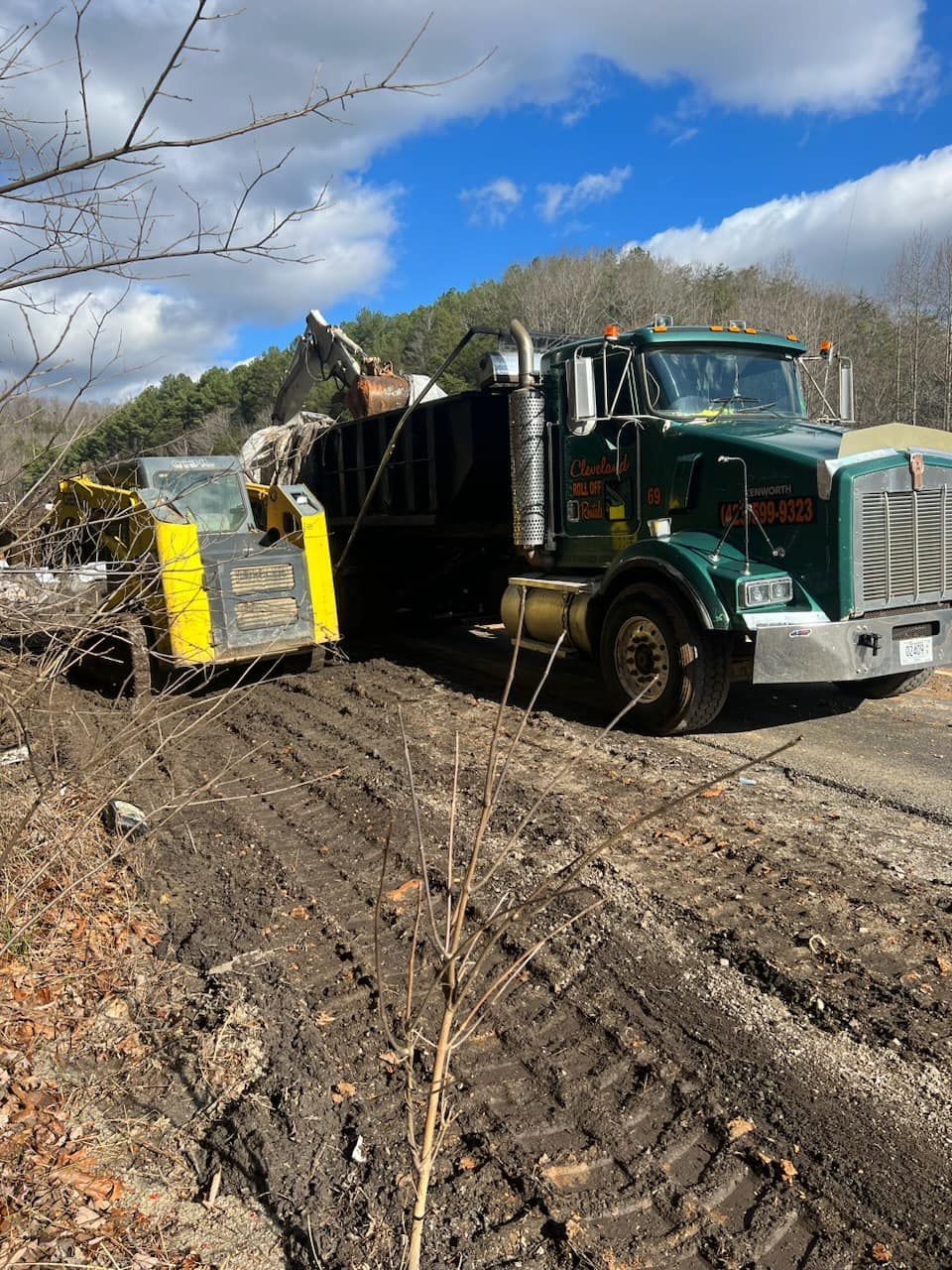A green dump truck being loaded with dirt and debris by an excavator.