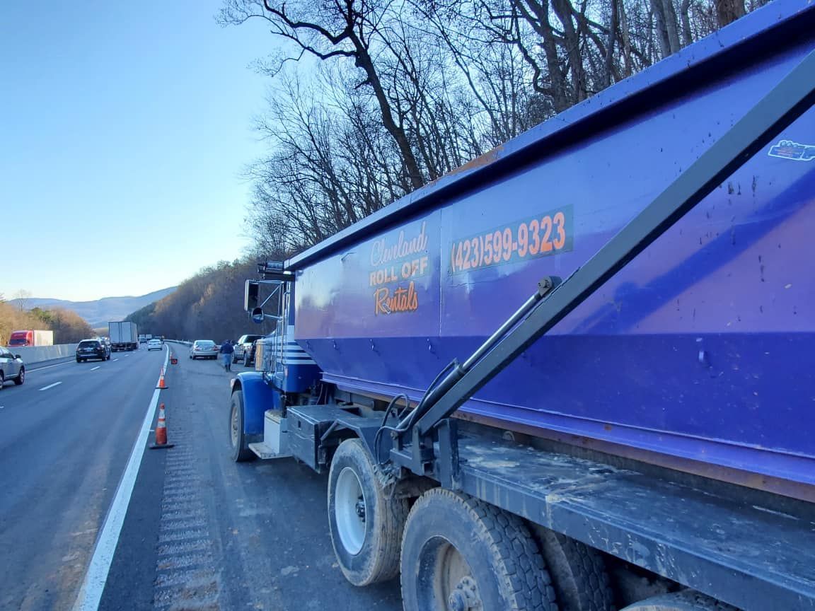 Blue dump truck on side of highway with traffic.